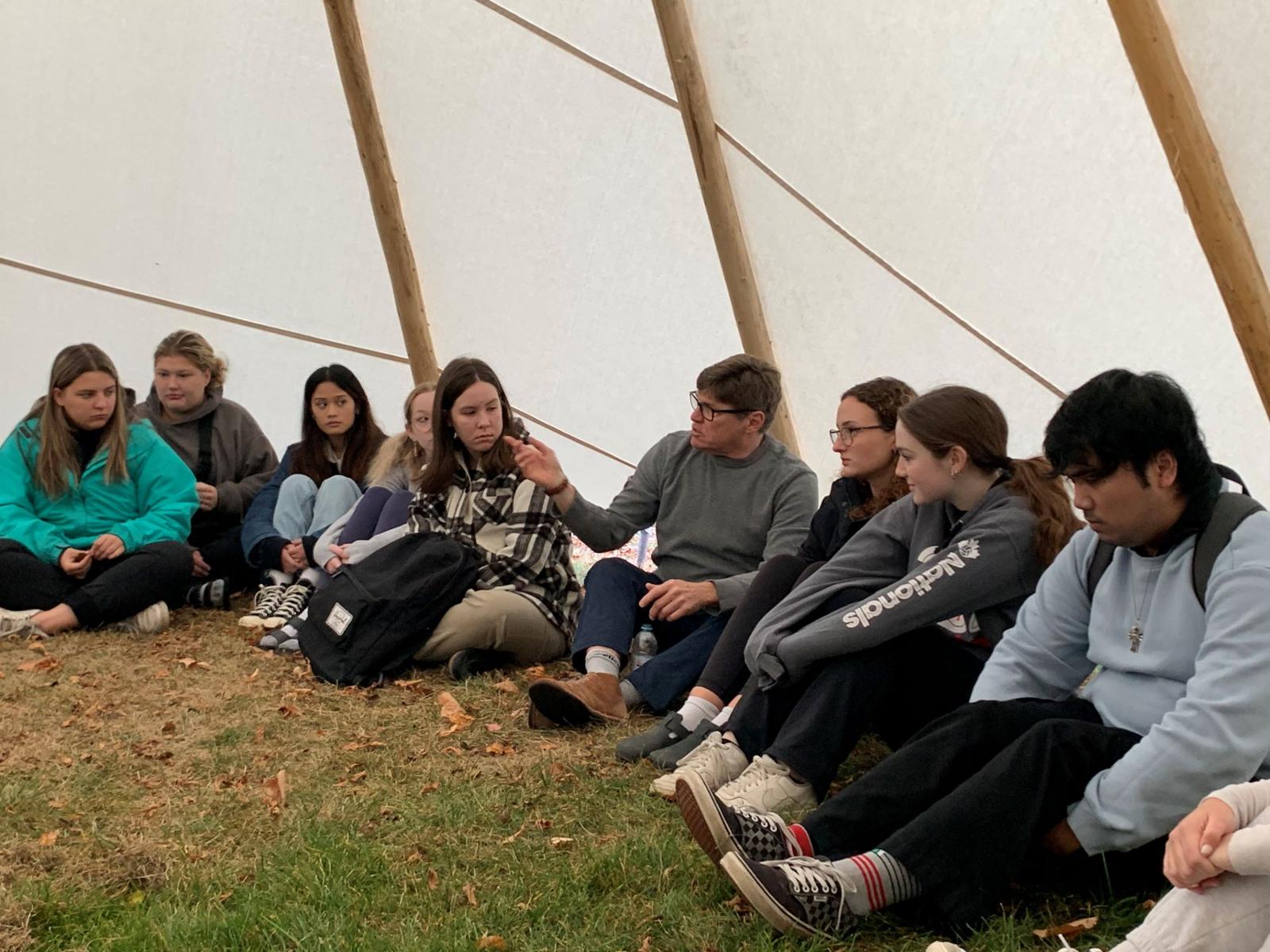 Students sit around a professor in a tipi classroom