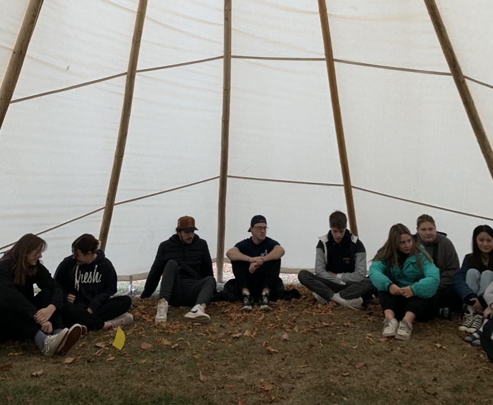 Students in a tipi listening to a professor