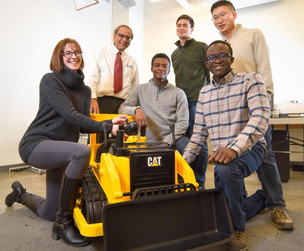 Six people surrounding a small bulldozer.