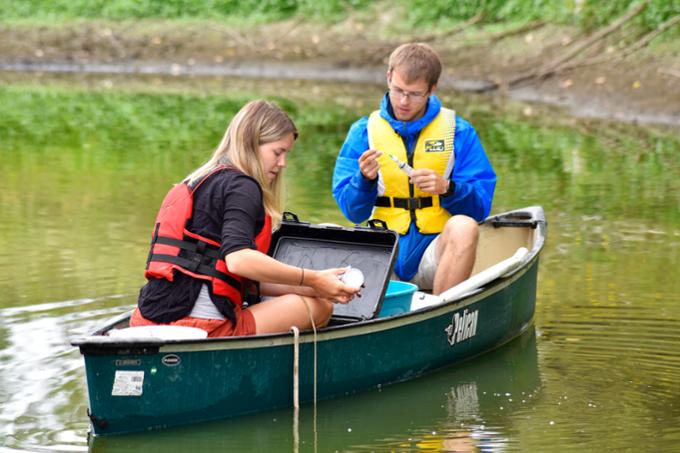 Two people in a canoe taking water samples from lake.