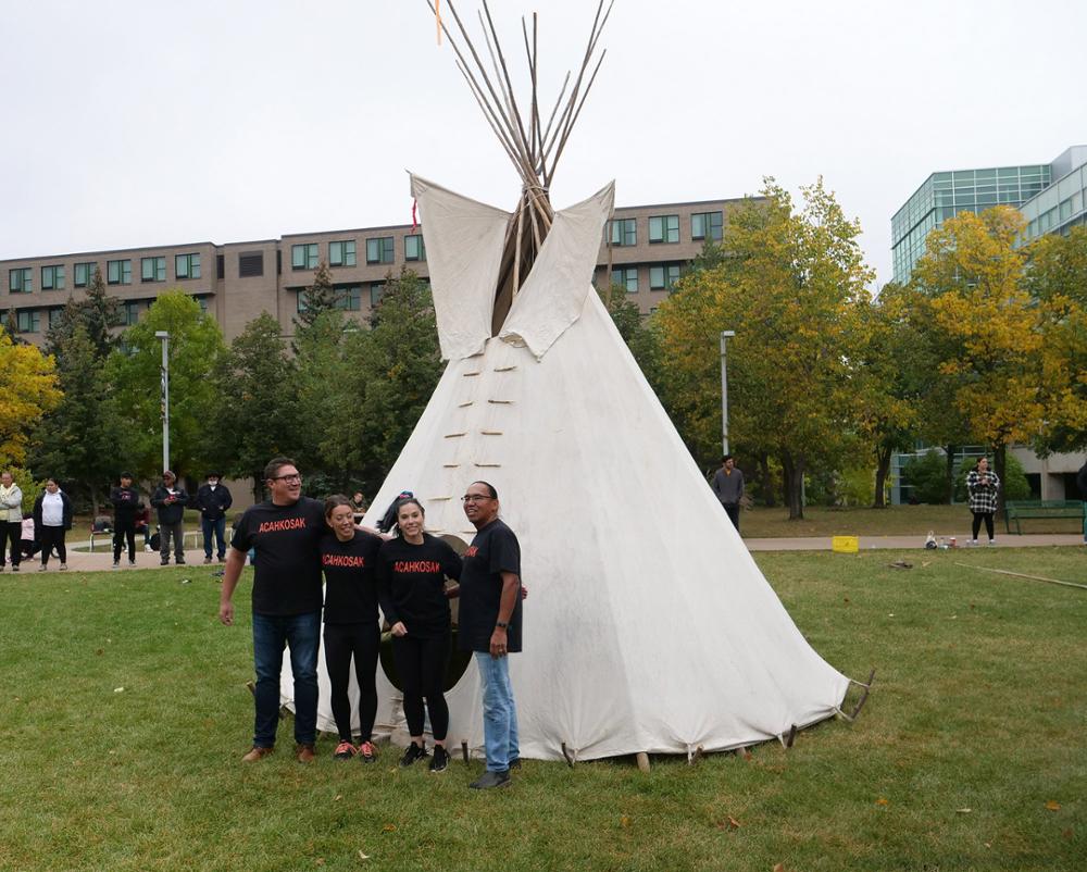 Four people standing in front of a tipi