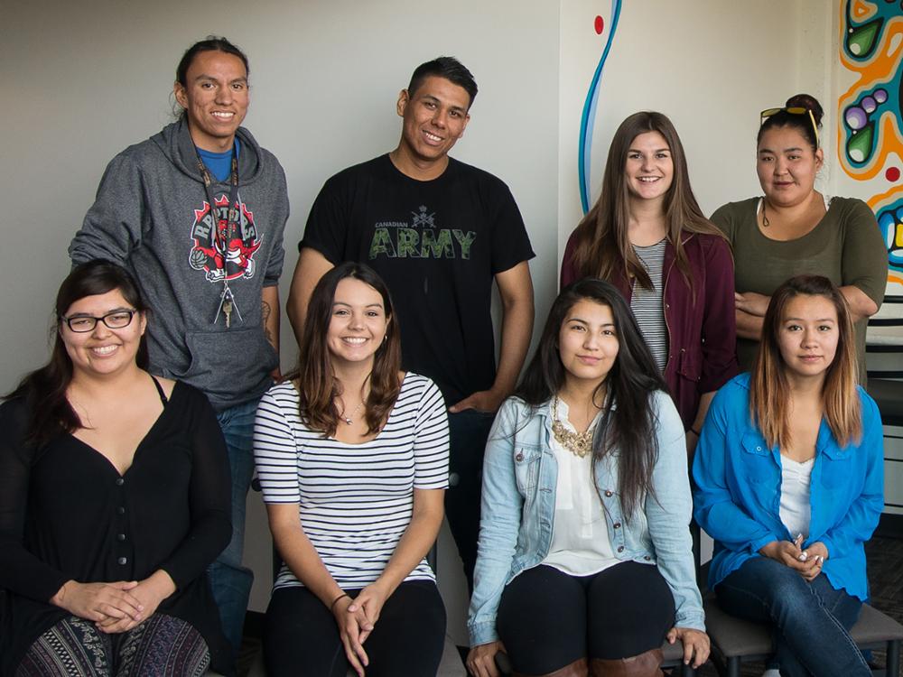 Eight people in front of Indigenous wall art within the Neekaneewak Living Learning Community.