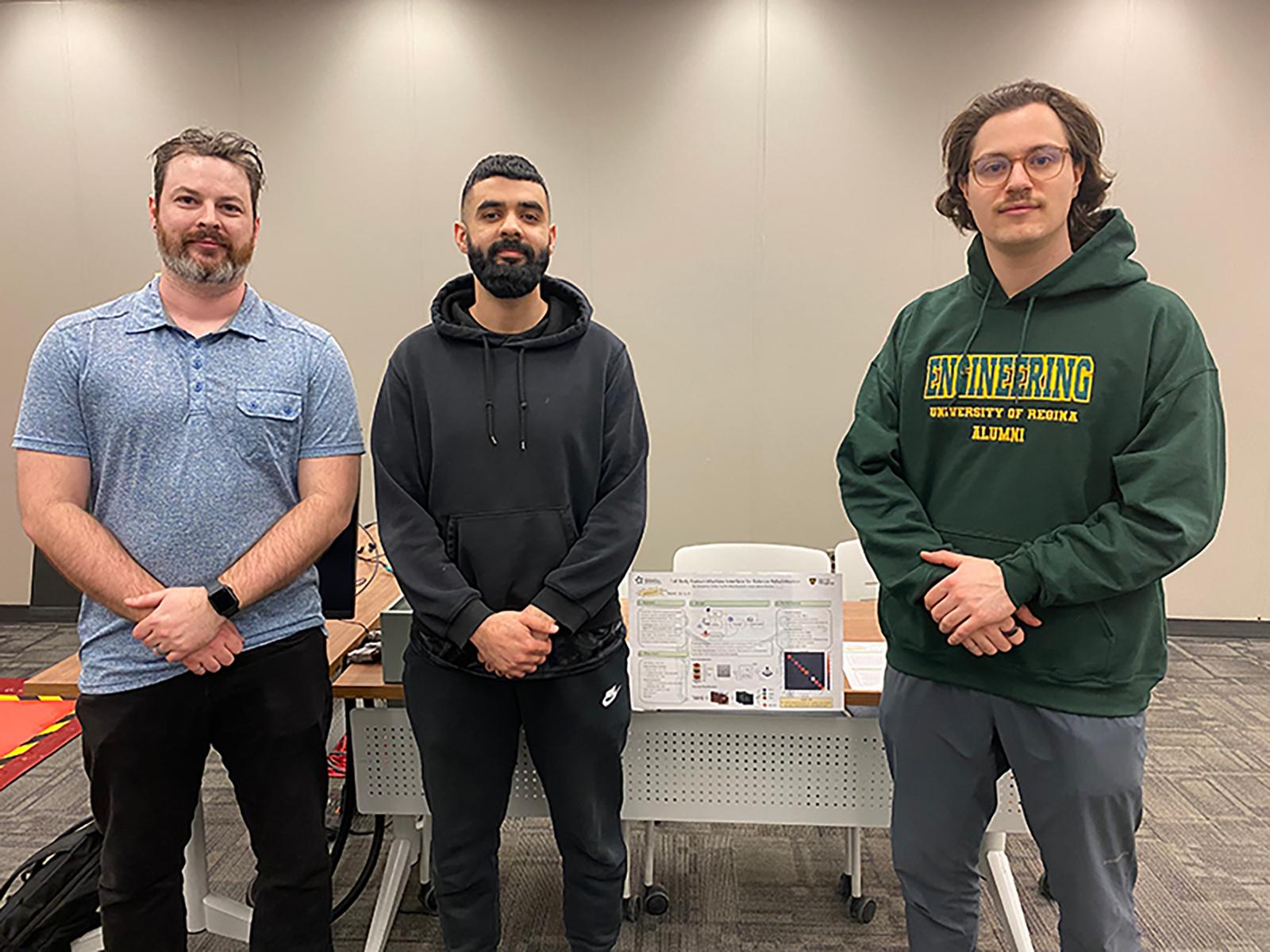 Three students stand in front of a project poster board