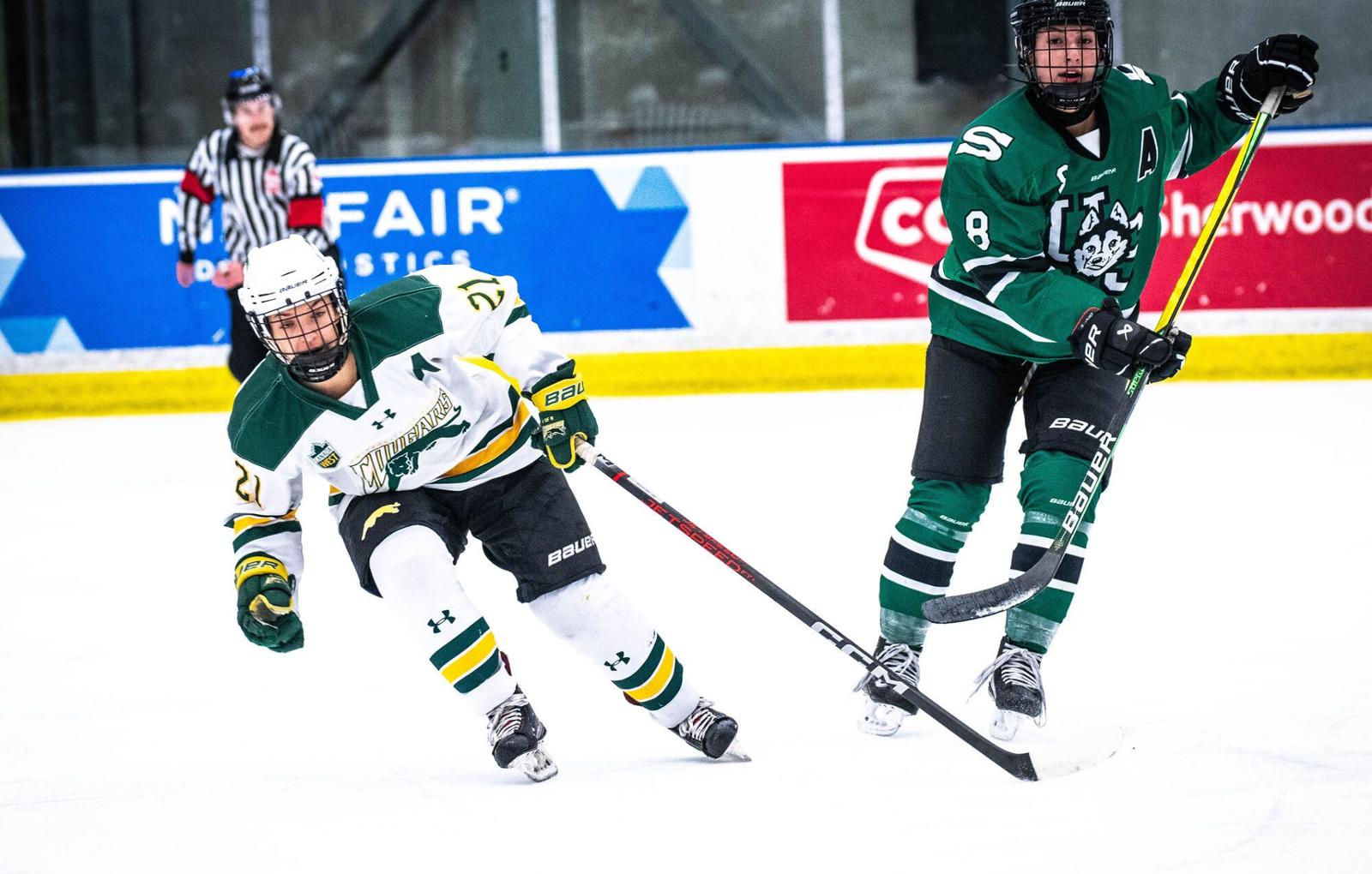 Two women hockey players from opposite teams chase a puck on an indoor hockey rink 