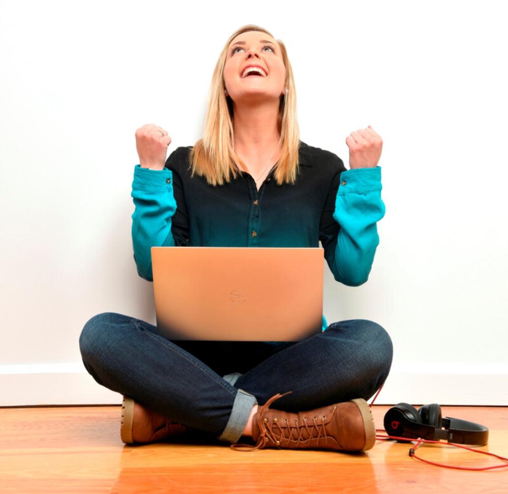 Female student seated with laptop and holding fists in air looking happy and proud of herself.