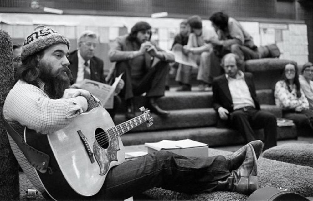 Black and white photo of individual sitting with a guitar.