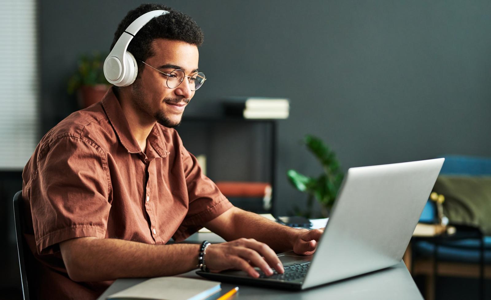 Individual sitting in front of a laptop with headphones on.