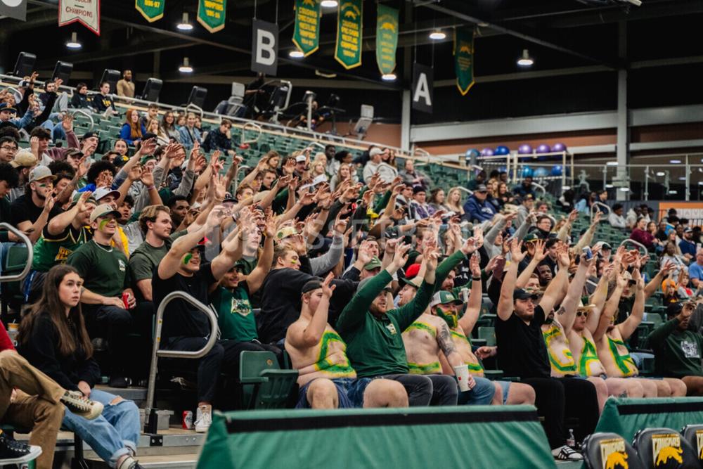 Large group of students in bleachers with hands raised.