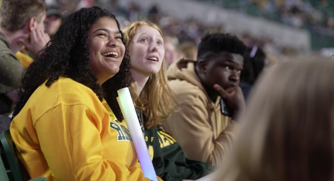 Close-up of two female students sitting in bleachers and smiling big.