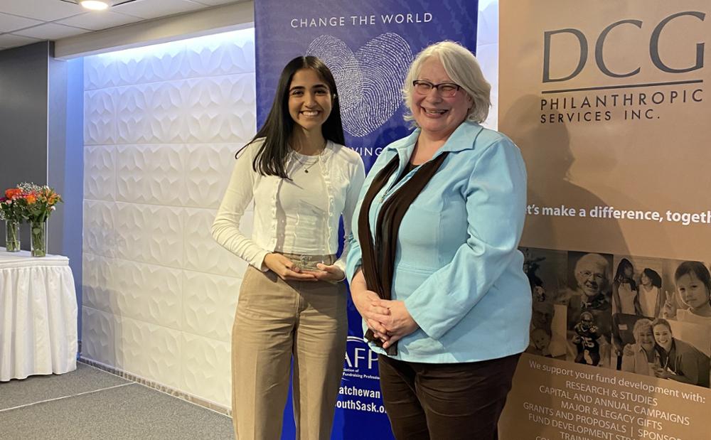 Two individuals standing side by side, one holding an award.