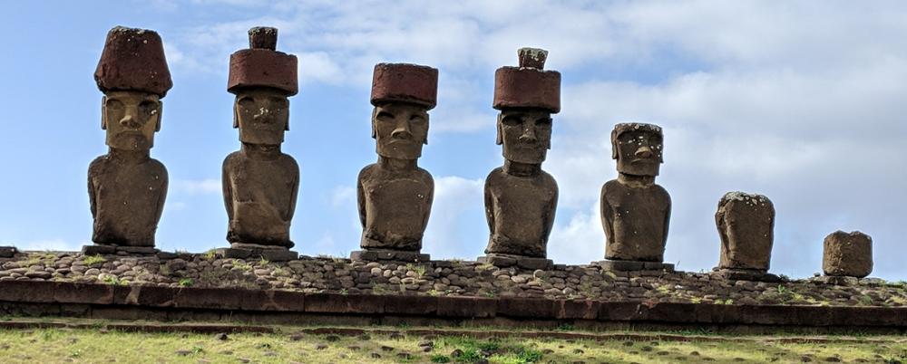 Photo of monolithic human figures carved from stone standing in a row on a hill.