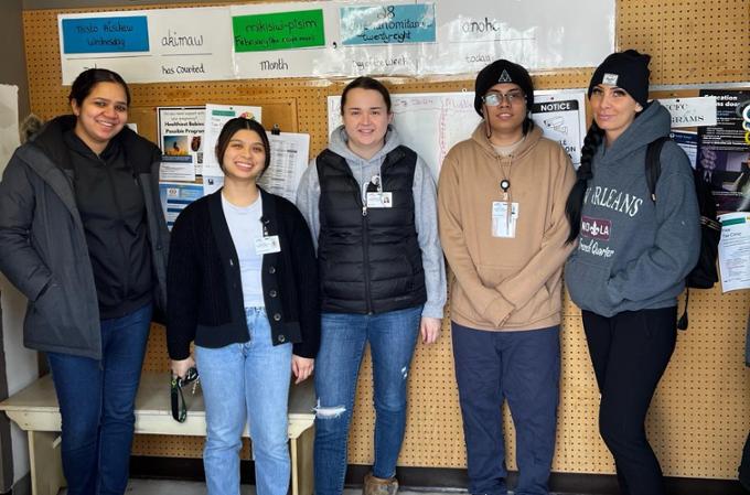 Five individuals in front of a bulletin board.