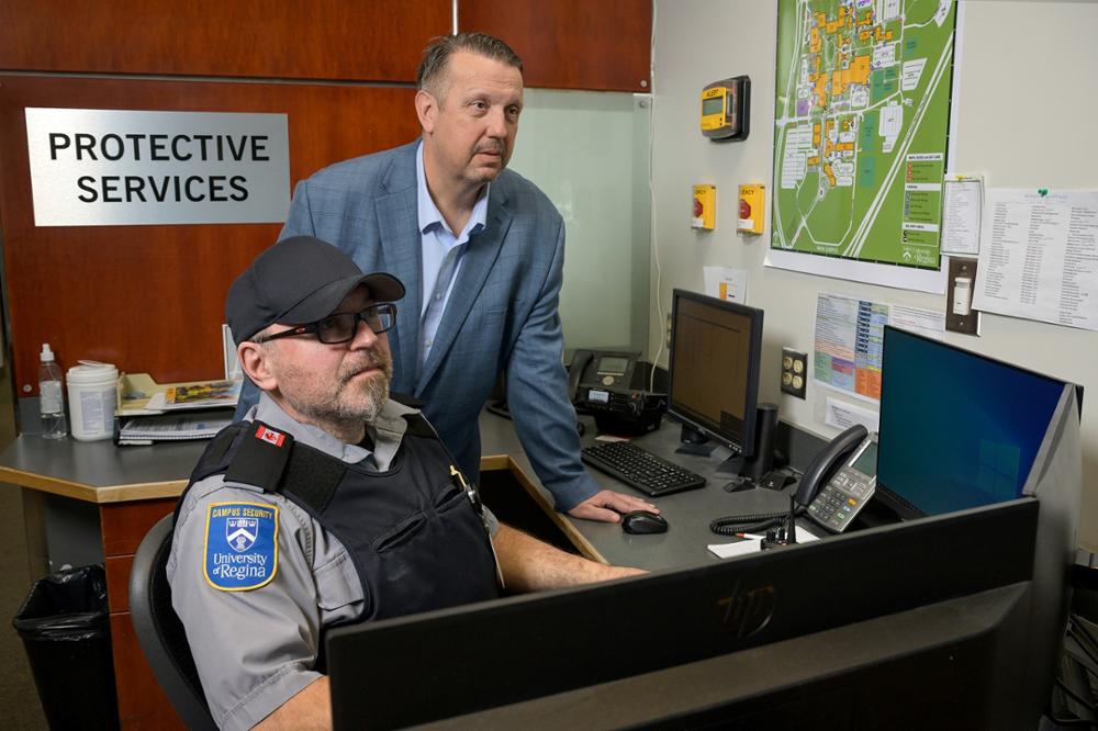 Two men, one sitting at a computer, the other looks at screen