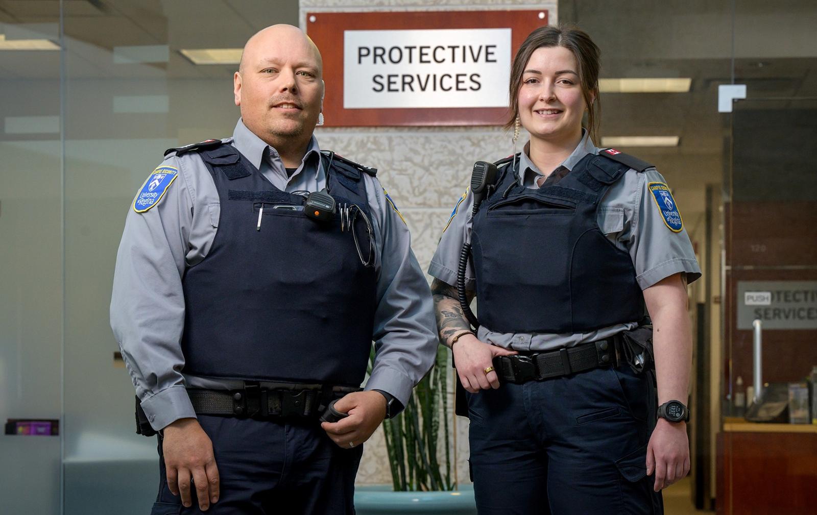 Two uniformed Protective Services officers pose in front of new signage.