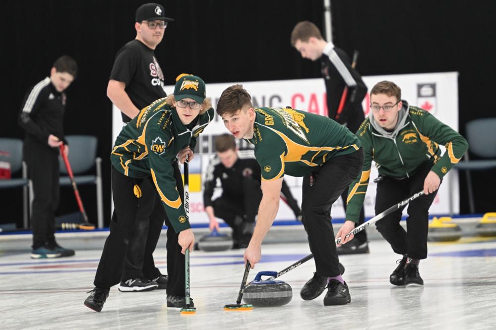 Two men on ice sweep curling rock with third man intently watching