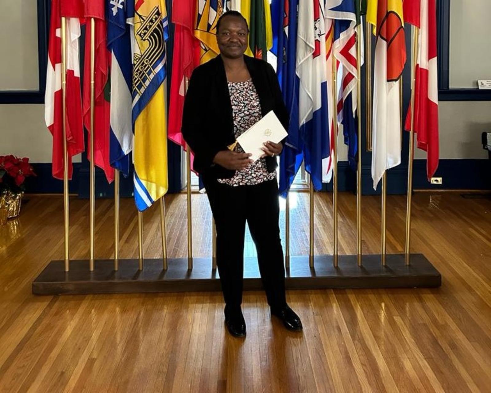 A woman stands in front of a number of Canadian provincial flags holding a certificate.