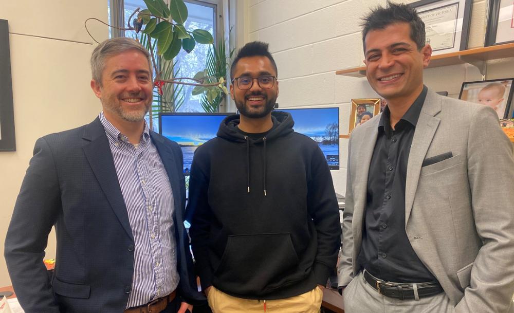 Three men standing in an office smiling at camera. 