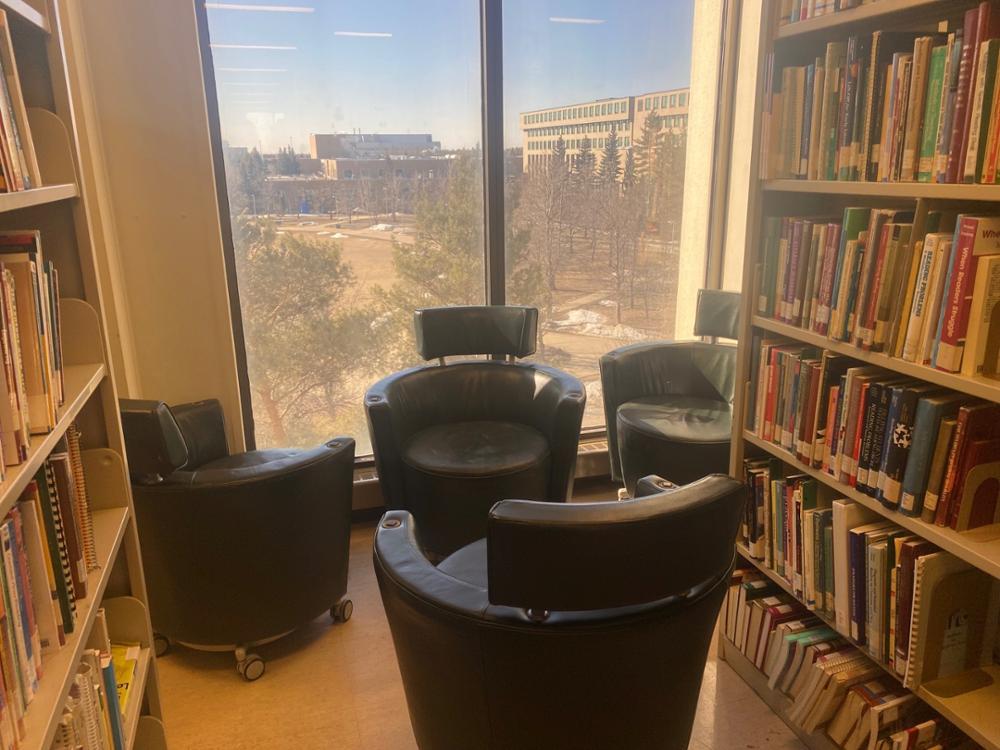 Four deep leather chairs by large window at the end of a book shelf on upper floor of the Library.