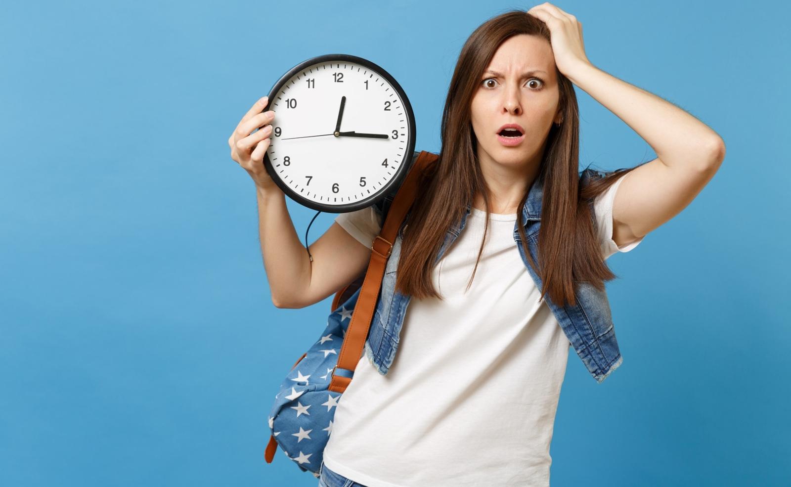 Female student with backpack holds clock and looks stressed as time ticks away.