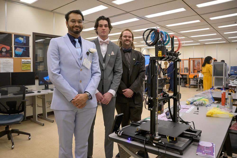 Three individuals standing beside their Engineering Capstone Project.