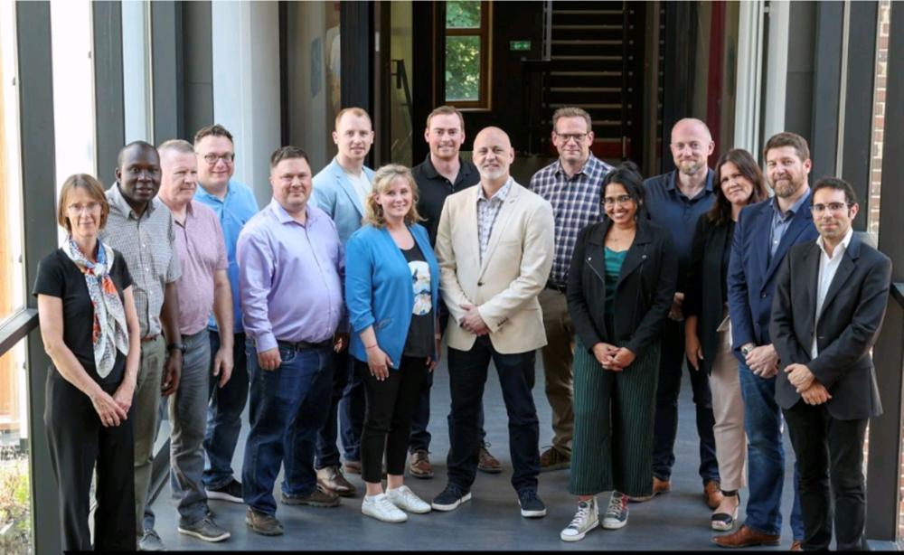 Group of professional men and women standing in a half circle and smiling in an atrium.