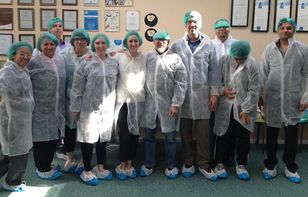 11 people standing close together in an office space personal protective equipment while smiling.