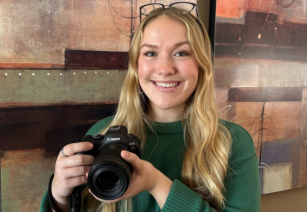 Young woman standing smiling and holding camera.