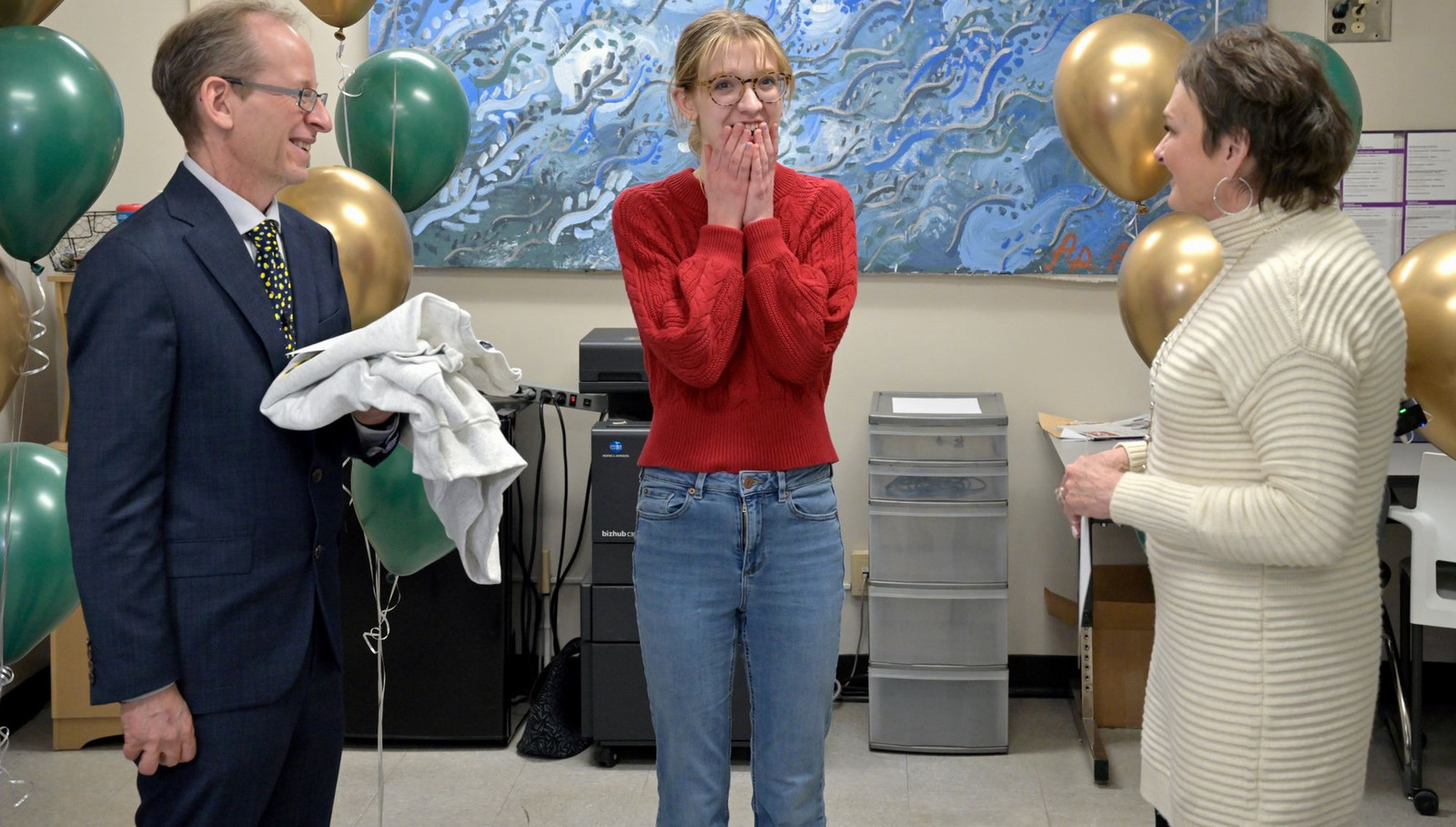 Woman stands between two people with hands raised to her face.