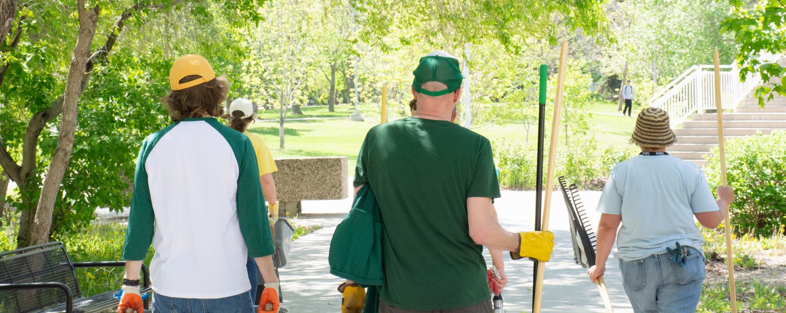 three people carrying rakes and shovels