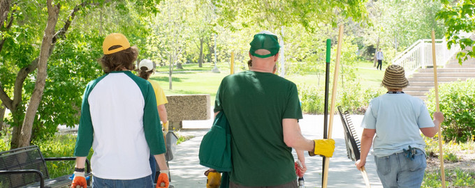 three people carrying rakes and shovels