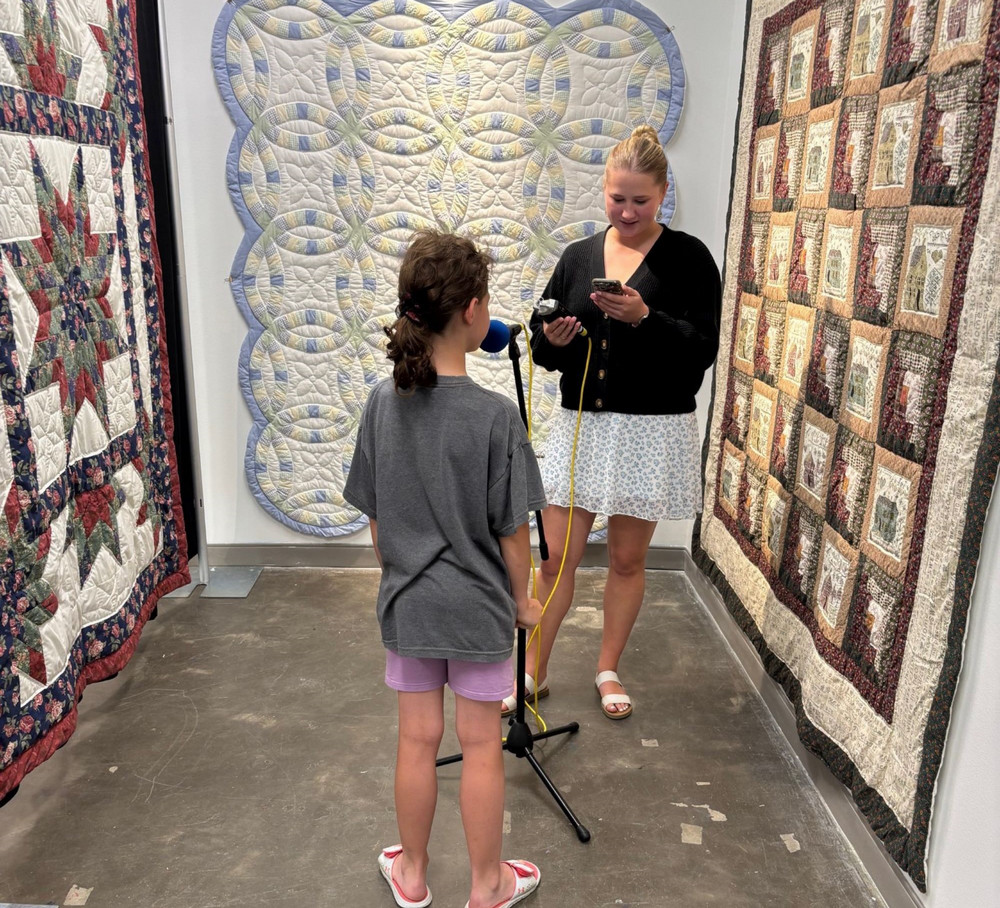 two people standing in front of quilts hanging on a wall