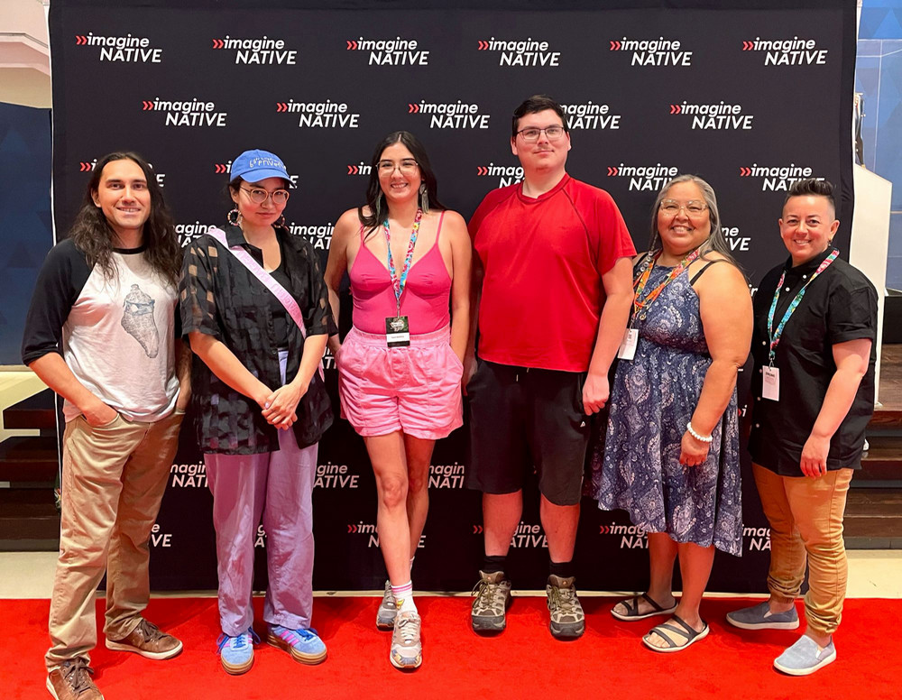 Six people standing on a red carpet and smiling