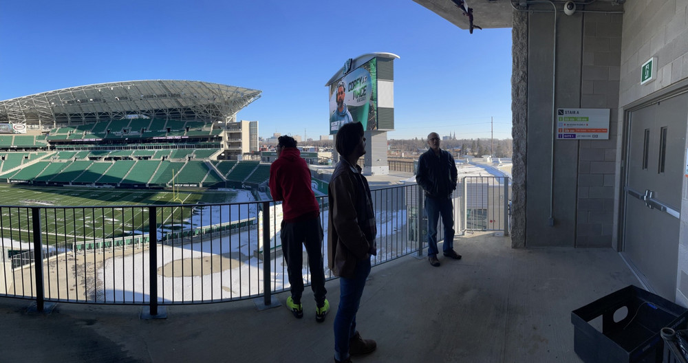 three people standing on a balcony in a stadium