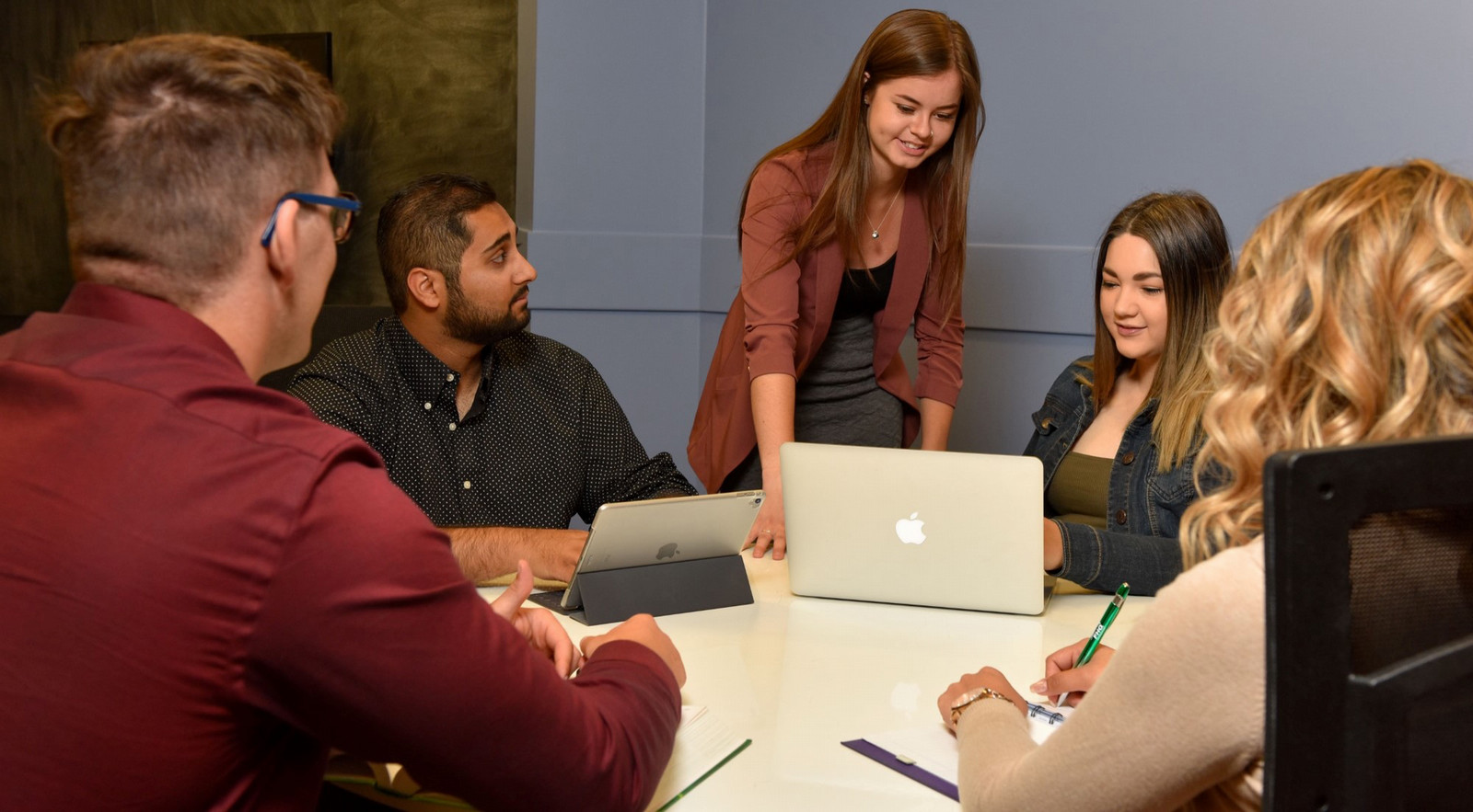 a group of five people sitting around a table looking at computers