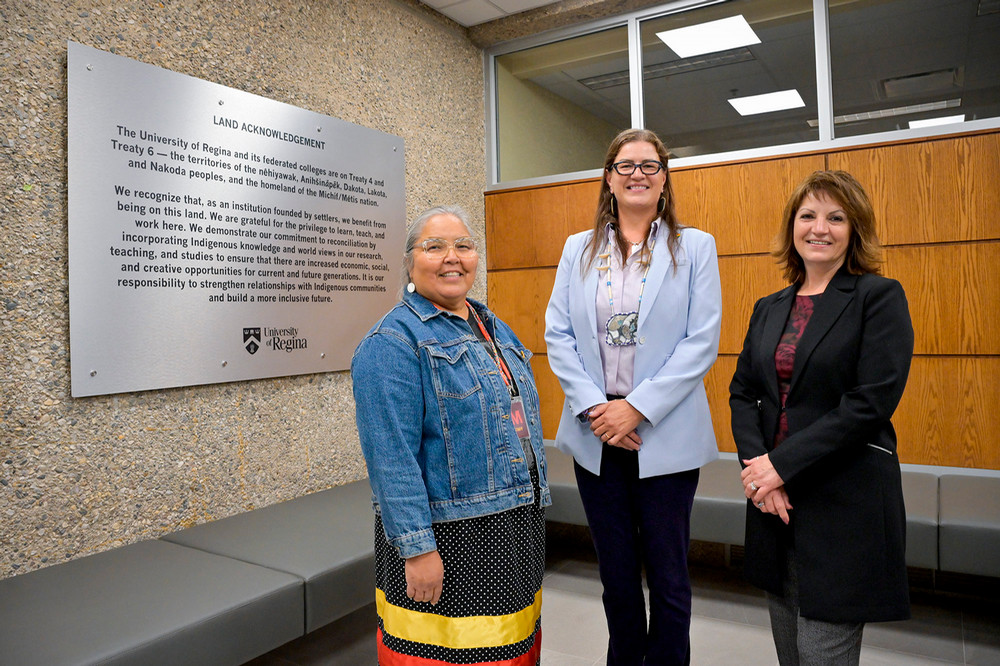 three people standing in front of a plaque on a wall
