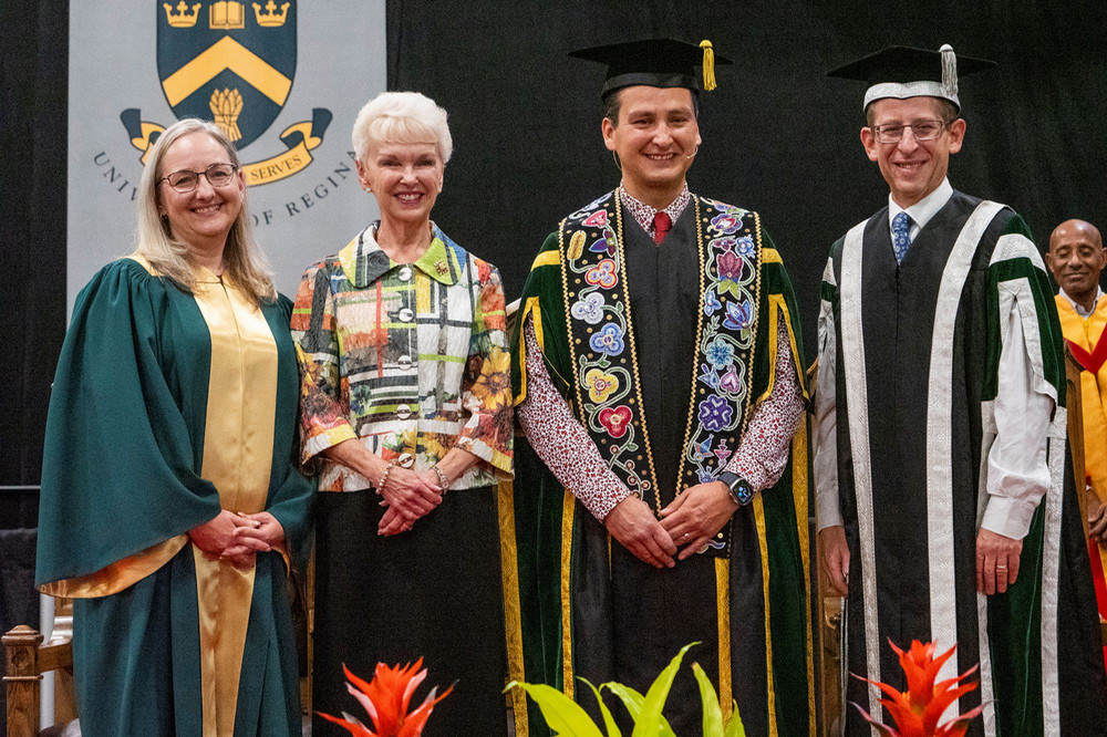 four people posing on stage at convocation