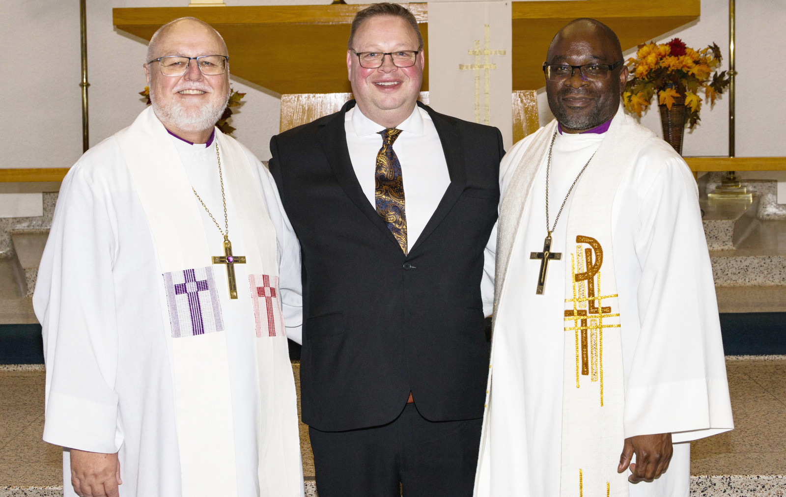 three smiling men standing on a church altar