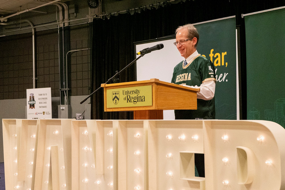 A man in a football jersey speaks at a podium. 