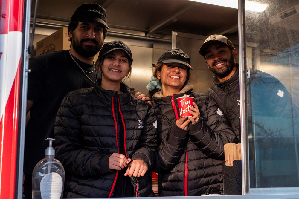four people stand in the window of a coffee truck. 
