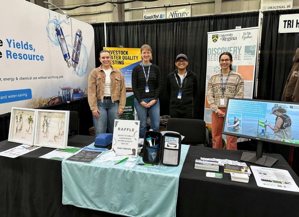 Four people stand together smiling at the University of Regina Biology booth at Agribition.