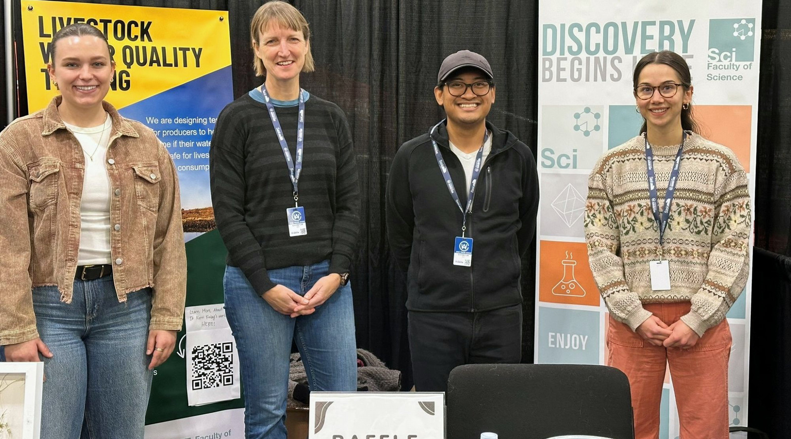 Four people stand together smiling at the University of Regina Biology booth at Agribition