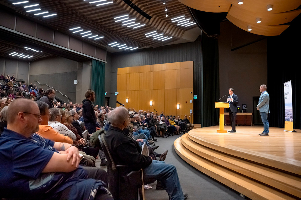 a wide shot of a large auditorium and a man speaking at a podium