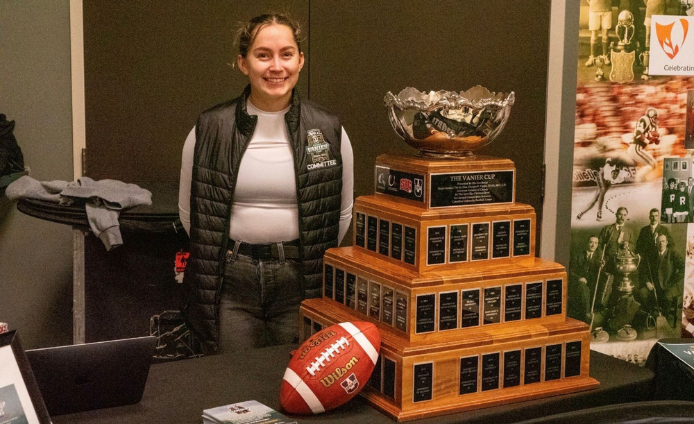 Young woman poses near a trophy and a football. 