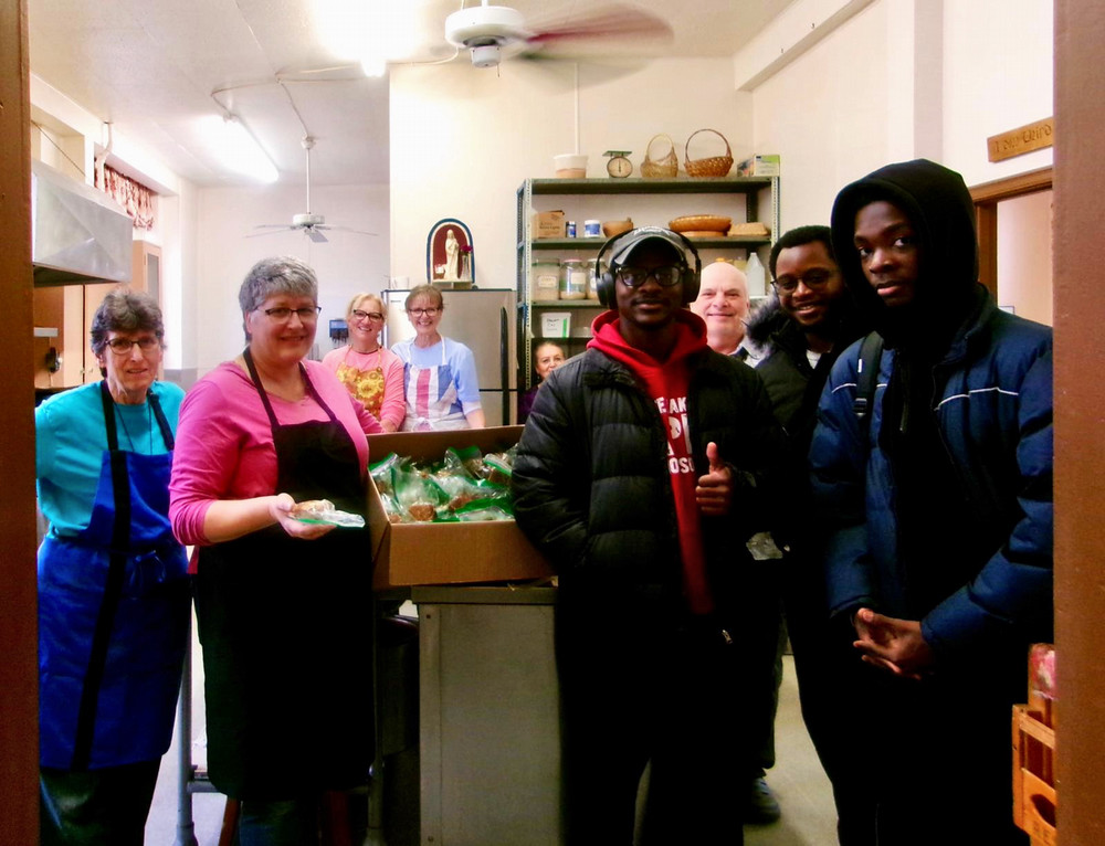 A group of people gather in a kitchen-like space. 