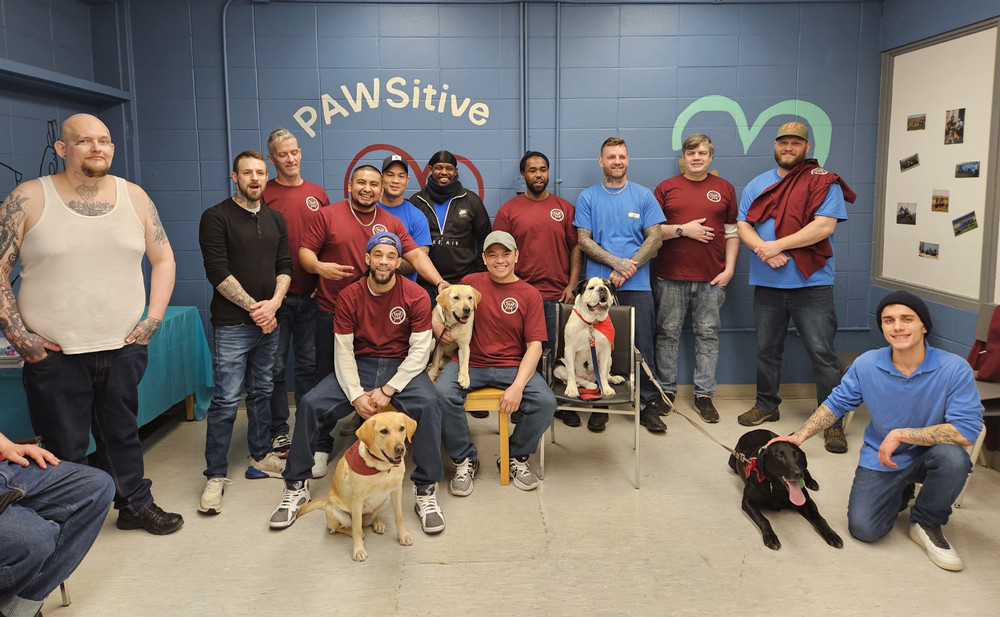 A group of people and dogs pose in a room in a prison.