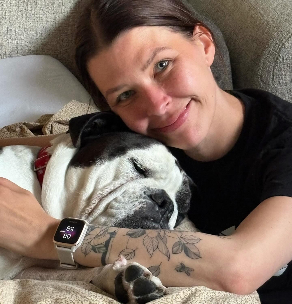 A smiling young woman cuddles a bulldog. 