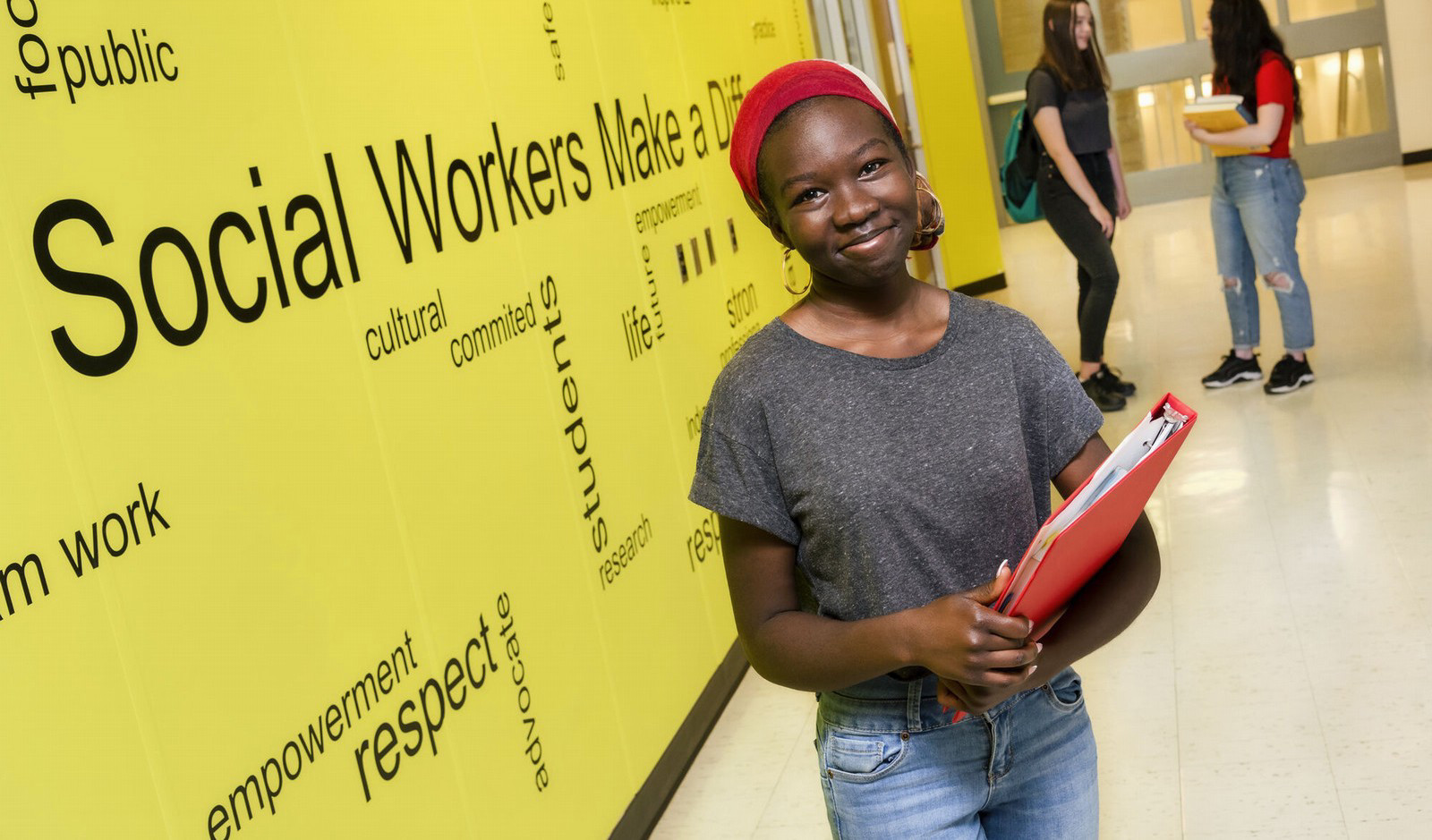 A young woman student stands in front of a Social Work sign. 