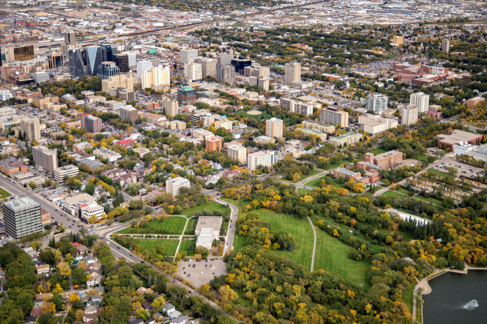 An aerial view of the City of Regina skyline featuring downtown high-rise buildings, the legislative dome, and the expansive Wascana Lake surrounded by autumn trees.