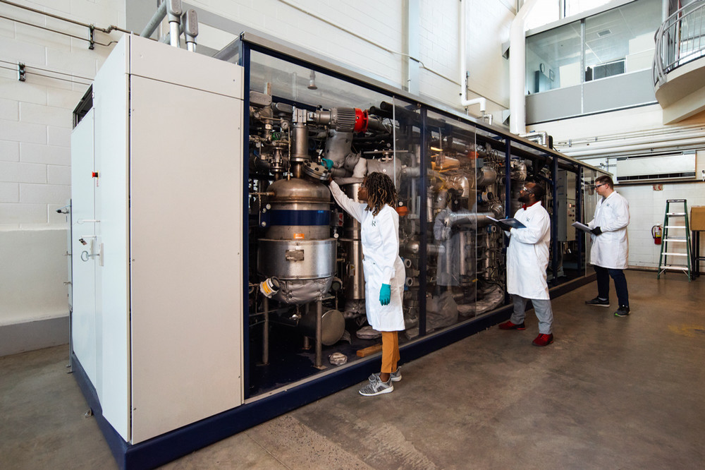 University of Regina researchers in lab coats examine and record data from large-scale research equipment inside a campus laboratory.