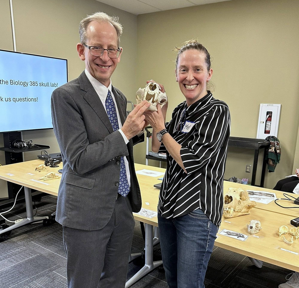 Two people holding a skull, with other skulls on a table